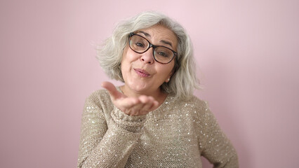 Middle age woman with grey hair blowing a kiss with hand over isolated pink background