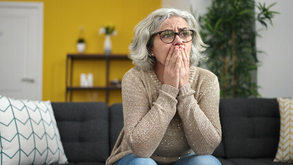 Middle age woman with grey hair stressed sitting on sofa at home