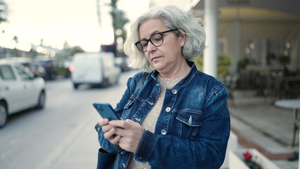 Middle age woman with grey hair using smartphone at street