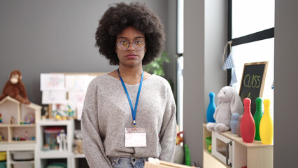 African american woman preschool teacher standing with relaxed expression at kindergarten
