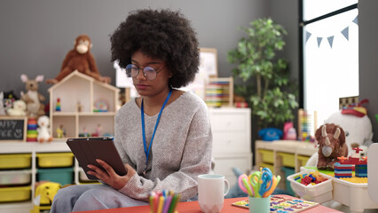African american woman preschool teacher writing on touchpad at kindergarten