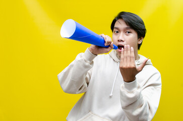 Shocked and surprised asian man shouting through paper megaphone giving an announcement.