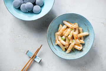 Turquoise bowls with korean traditional rice cakes tteokbokki and mochi, top view on a light-beige stone background, horizontal shot