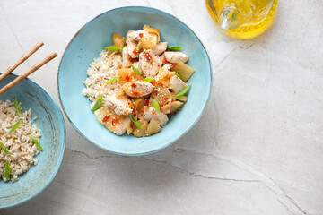 Chicken and kimchi stir-fry with brown rice served in turquoise bowls, top view on a beige stone background, horizontal shot with space