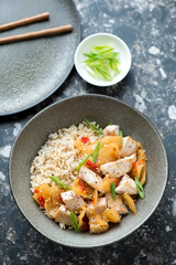 Olive bowl with korean chicken and kimchi stir-fry, vertical shot on a dark-brown granite background, elevated view