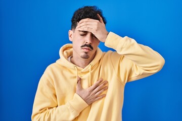 Hispanic man standing over blue background touching forehead for illness and fever, flu and cold, virus sick