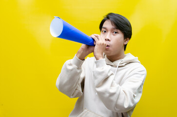 Shocked and surprised asian man shouting through paper megaphone giving an announcement.