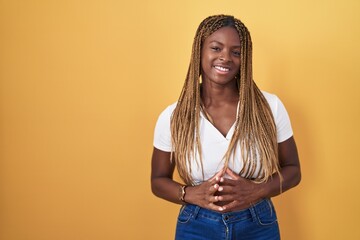 African american woman with braided hair standing over yellow background hands together and fingers crossed smiling relaxed and cheerful. success and optimistic