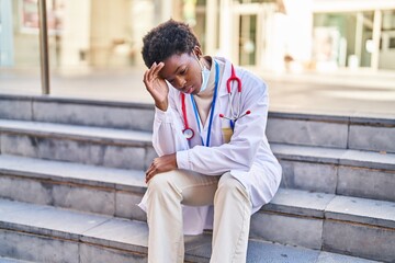 African american woman wearing doctor uniform and medical mask with worried expression at street