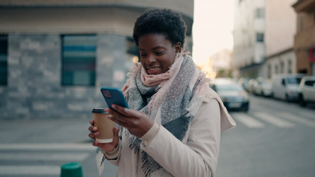 Young african american woman using smartphone drinking coffee at street