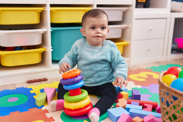 Adorable hispanic baby playing with hoops game sitting on floor at kindergarten