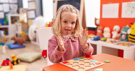 Adorable blonde girl playing with maths puzzle game clapping hand at kindergarten