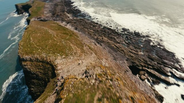 FPV Aerial view of waves crashing onto a rocky coastline at Worm's Head on the Gower peninsula of Wales with a FPV drone