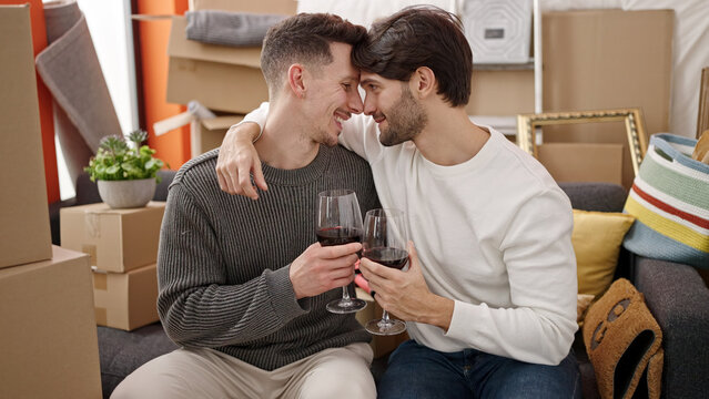 Two men couple drinking glass of wine at new home