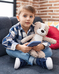 Adorable caucasian boy hugging teddy bear using smartphone at home