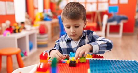 Adorable caucasian boy playing with construction blocks sitting on table at kindergarten