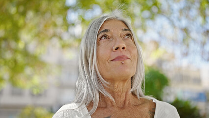 Middle age grey-haired woman looking to the sky with serious expression at park