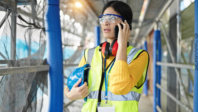 Young beautiful hispanic woman architect talking on smartphone at street