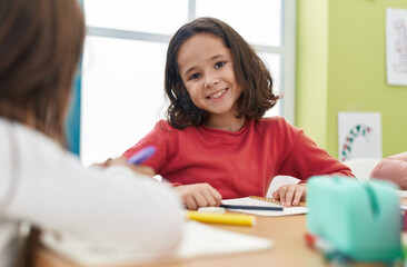 Adorable hispanic girl student writing on notebook at classroom