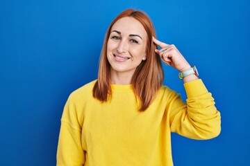 Fototapeta premium Young woman standing over blue background smiling pointing to head with one finger, great idea or thought, good memory