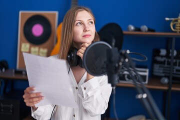 Young caucasian woman artist reading song with doubt expression at music studio