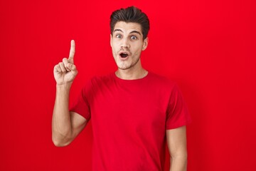 Young hispanic man standing over red background pointing finger up with successful idea. exited and happy. number one.