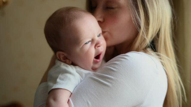 A loving mother holds, hugs, kisses her baby, the mother looks at her child with love and tenderness. Care and childcare
