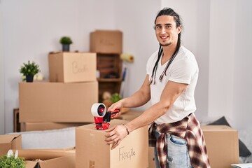Fototapeta na wymiar Young man smiling confident packing cardboard box at new home