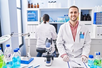 Young man working at scientist laboratory looking positive and happy standing and smiling with a confident smile showing teeth