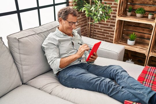 Middle age man using touchpad sitting on sofa at home