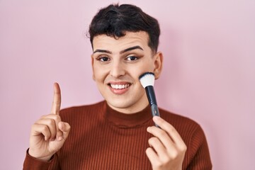 Non binary person applying make up smiling with an idea or question pointing finger with happy face, number one