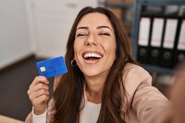 Young brunette woman working at small business ecommerce holding credit card smiling and laughing...