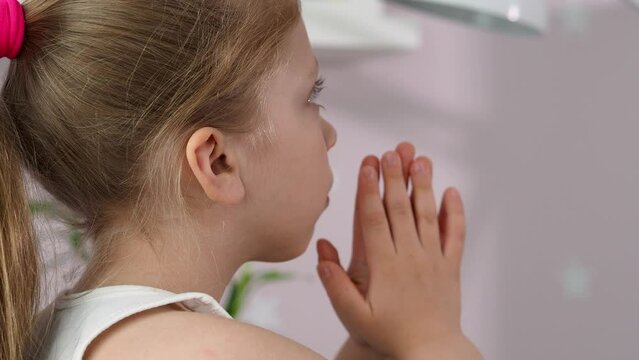 Cute little girl praying at home. Hands folded in prayer concept of faith, worship, spirituality and religion. The child desperately asks for help. A sad child lies on the table and prays to God.