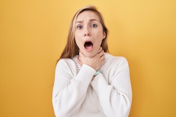 Young caucasian woman wearing white sweater over yellow background shouting suffocate because painful strangle. health problem. asphyxiate and suicide concept.