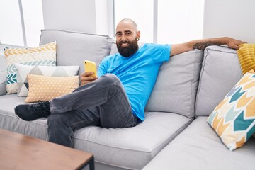 Young bald man using smartphone sitting on sofa at home