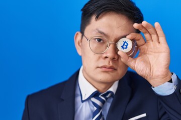 Fototapeta na wymiar Young asian man holding virtual currency bitcoin covering eye relaxed with serious expression on face. simple and natural looking at the camera.