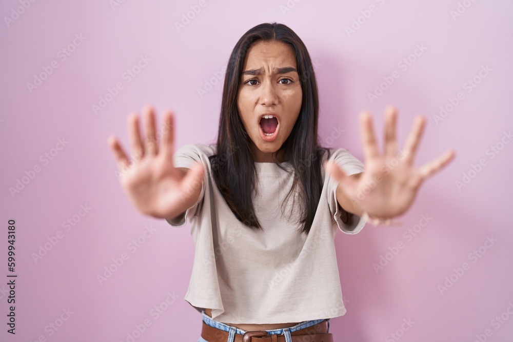 Canvas Prints Young hispanic woman standing over pink background doing stop gesture with hands palms, angry and frustration expression