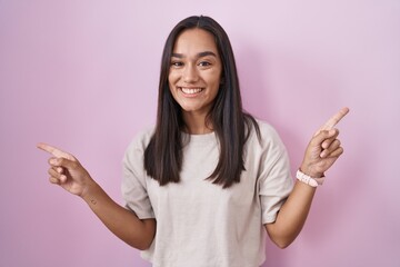 Young hispanic woman standing over pink background smiling confident pointing with fingers to different directions. copy space for advertisement