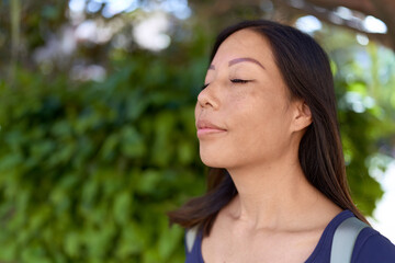 Young asian woman breathing with closed eyes at park