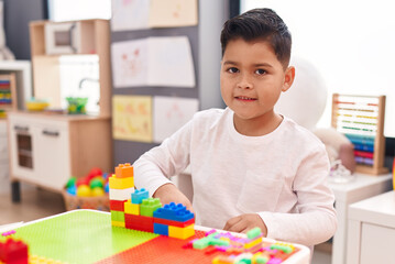 Adorable hispanic boy playing with construction blocks sitting on table at kindergarten