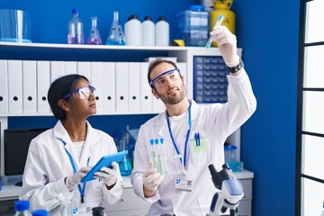 Man and woman scientists using touchpad holding test tubes at laboratory