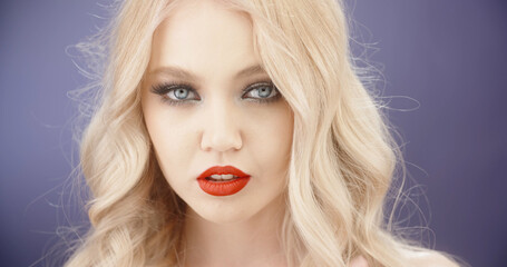 Sensual blonde caucasian girl with bright makeup looking at camera with seductive stare - close up shot 