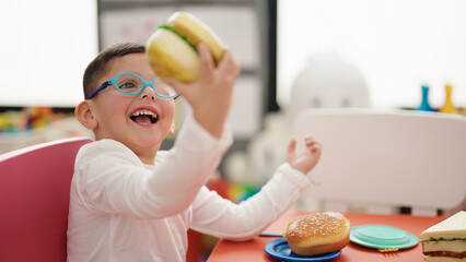 Adorable hispanic boy playing with hamburger toy at kindergarten