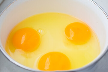 Three egg yolks and whites in a bowl