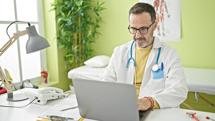 Middle age man doctor using laptop working at clinic