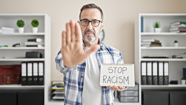 Middle age man business worker holding stop racism notebook at office
