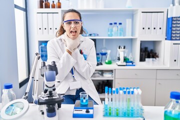 Young hispanic woman working at scientist laboratory shouting and suffocate because painful...