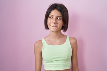Young girl standing over pink background smiling looking to the side and staring away thinking.