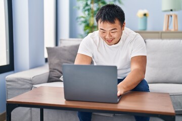Fototapeta premium Young chinese man using laptop sitting on sofa at home
