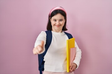 Woman with down syndrome wearing student backpack and holding books approving doing positive gesture with hand, thumbs up smiling and happy for success. winner gesture.